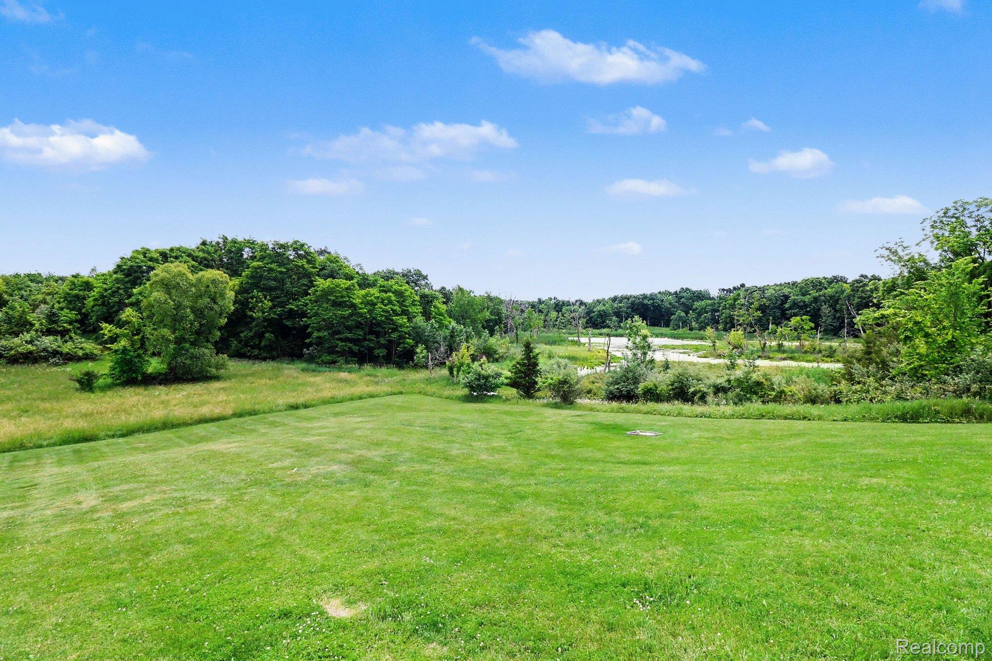 18501 Taylor Lake Road Holly, MI 48442 - Photo 33 of 35 Expansive green lawn with a backdrop of mature trees and a distant body of water