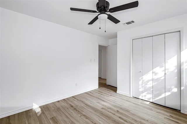 an empty room with wooden floor fan and windows