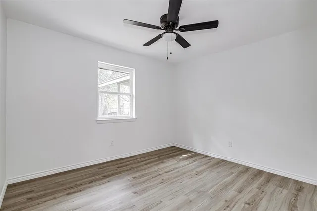 an empty room with wooden floor ceiling fan and window