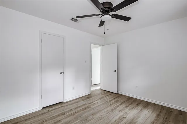 an empty room with wooden floor fan and windows