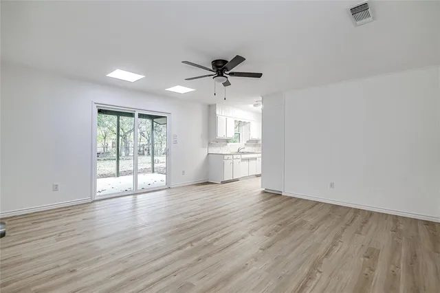 an empty room with wooden floor chandelier fan and windows