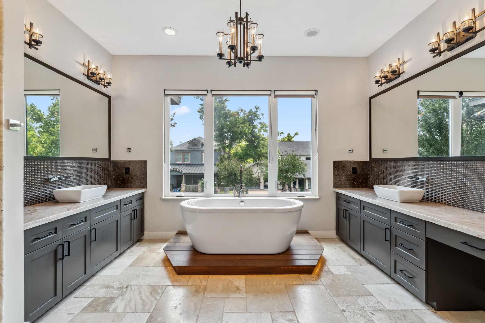 815 East 27th Street Houston, TX 77009 - Photo 22 of 44 As you step through double doors into the luxurious Primary Bathroom, you’re greeted by the stunning pedestal tub set on a wood riser w/ accent lighting, complemented by a chandelier above for added ambiance.The large windows are outfitted with pull down blackout shades. 2 large vanities with ample storage,along with tile backsplashes,vessel sinks, & wall-mounted faucets,elevate the space.Decorative mirrors & vanity lights enhance the overall design, while dedicated knee space at each vanity adds function.