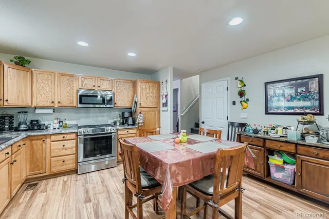 a open kitchen with stainless steel appliances granite countertop a stove top oven a refrigerator a sink dishwasher a dining table and chairs with wooden floor