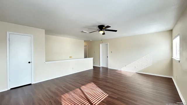 an empty room with wooden floor fan and windows