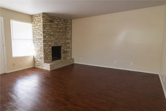 an empty room with wooden floor fire place and windows
