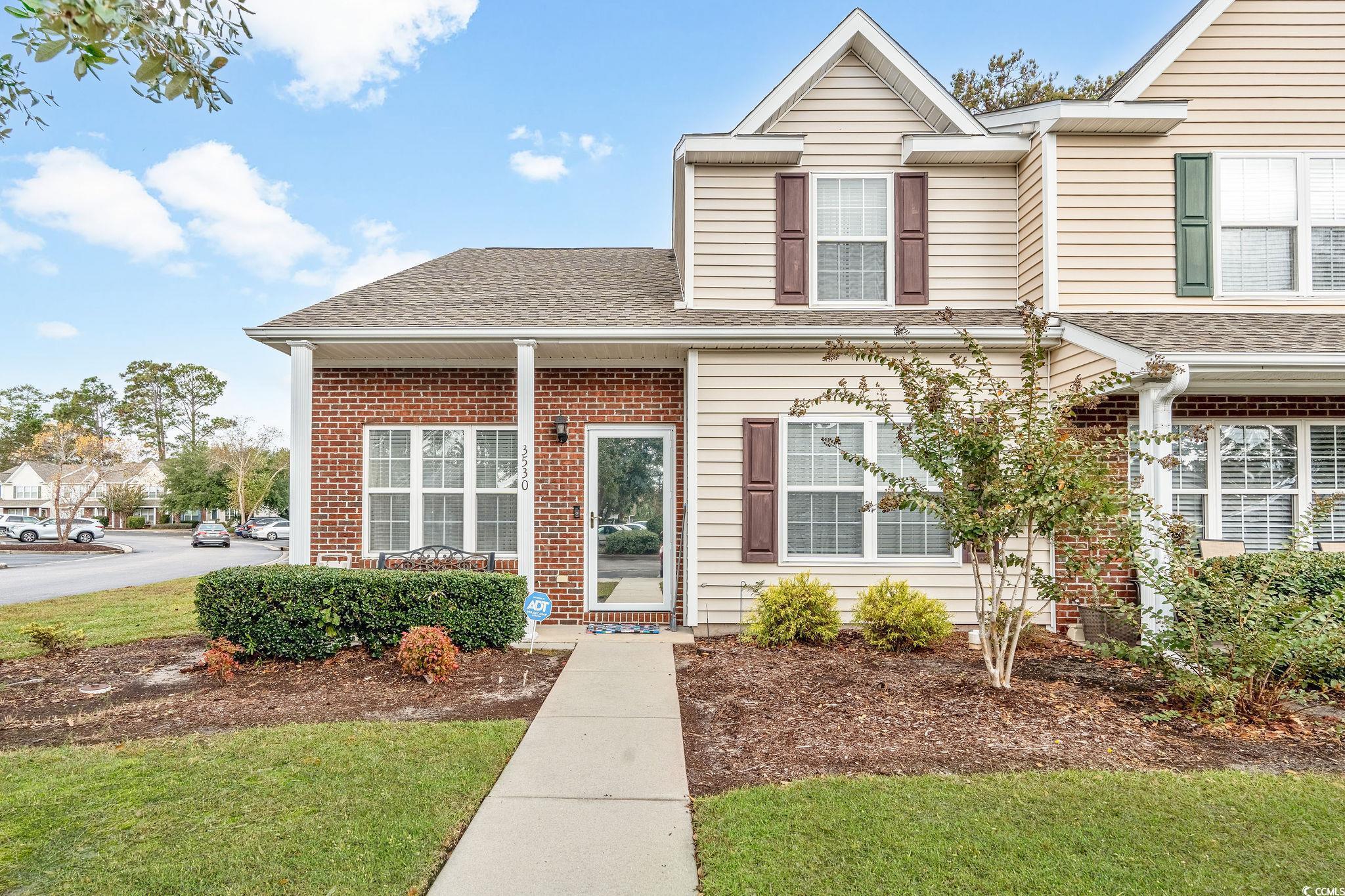 Traditional home featuring a shingled roof, brick siding, a front lawn, and covered porch