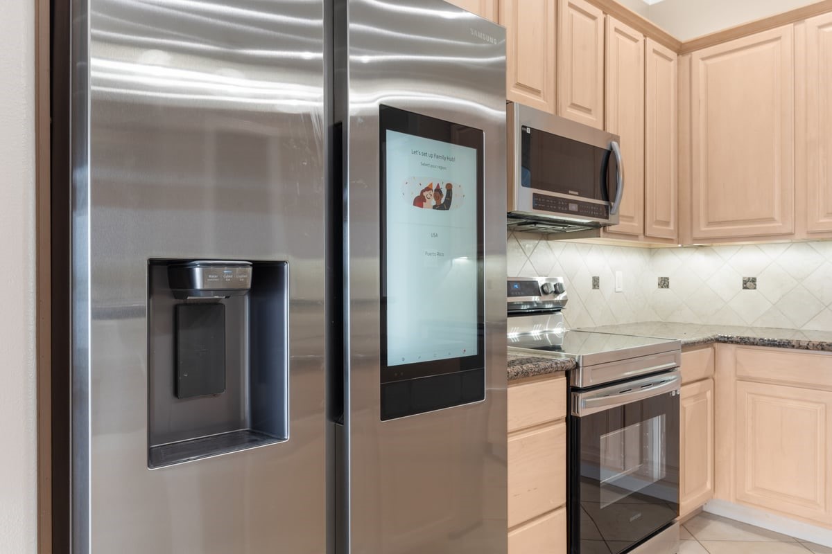 168 Lake Point Boulevard, Unit C102 Conroe, TX 77356 - Photo 6 of 35 Modern kitchen featuring stainless steel appliances, including a smart fridge with a touchscreen, microwave, and oven, complemented by light wood cabinets and granite countertops.