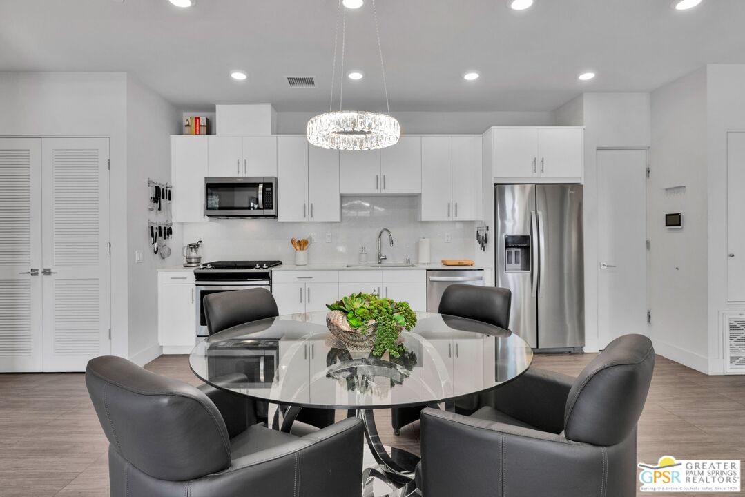 138 The River Palm Springs, CA 92262 - Photo 13 of 47 a kitchen with stainless steel appliances kitchen island granite countertop a refrigerator a stove a sink dishwasher a dining table and chairs with wooden floor