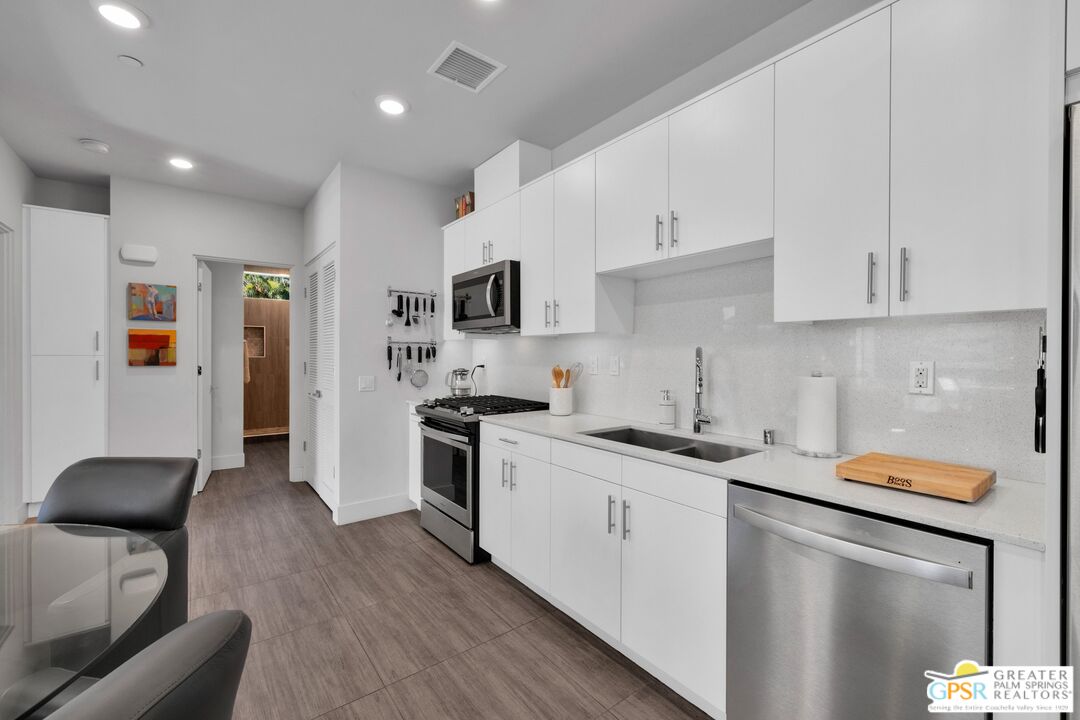 138 The River Palm Springs, CA 92262 - Photo 14 of 47 a kitchen with stainless steel appliances granite countertop a stove top oven a sink a refrigerator white cabinets and wooden floor