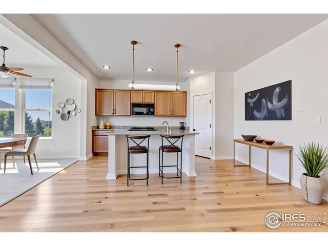 a kitchen with stainless steel appliances kitchen island granite countertop a refrigerator a stove a sink a dining table and chairs with wooden floor