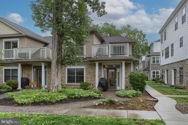 a view of a brick house with a yard plants and large tree