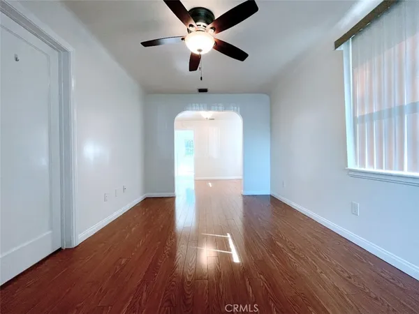 an empty room with wooden floor chandelier fan and windows
