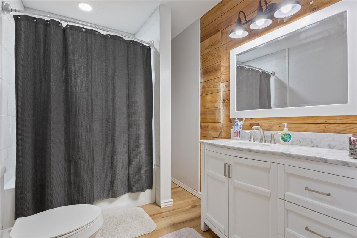 1607 North Harding Avenue Cameron, TX 76520 - Photo 29 of 37 A well-appointed bathroom features a pristine white vanity, a large mirror, and warm wood paneling.