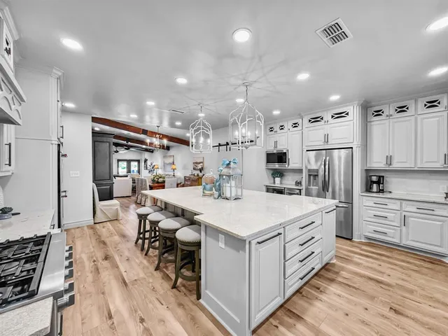 a large kitchen with kitchen island a sink a stove a refrigerator and white cabinets with wooden floor