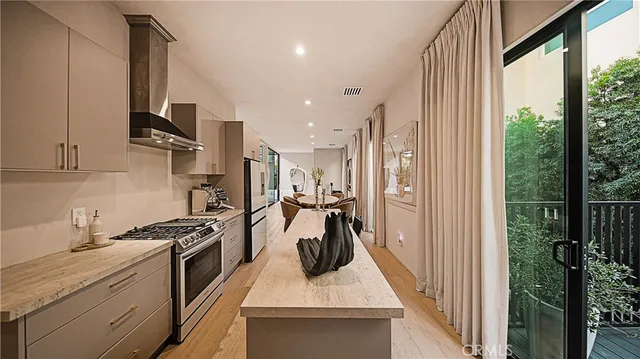 a kitchen with stainless steel appliances granite countertop a refrigerator a sink dishwasher a stove and a dining table with wooden floor