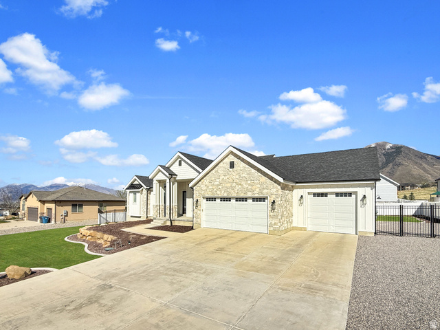 916 Rocky Mountain Way Elk Ridge, UT 84651 - Photo 4 of 54 View of front of house featuring an attached garage, concrete driveway, a mountain view, stone siding, and a shingled roof