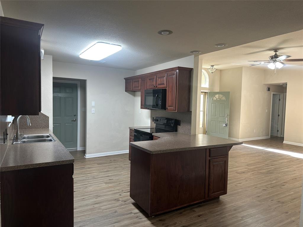 208 Pearl Drive Hewitt, TX 76643 - Photo 5 of 17 Kitchen with dark brown cabinets, black appliances, a peninsula, dark countertops, and light wood finished floors