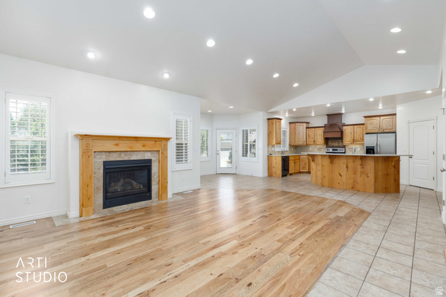 2327 Bluff Ridge Drive Syracuse, UT 84075 - Photo 12 of 66 Open-concept living space featuring wood-finish flooring, a fireplace with a wood mantel and stone surround, and an adjacent kitchen with wood cabinetry and stainless steel appliances