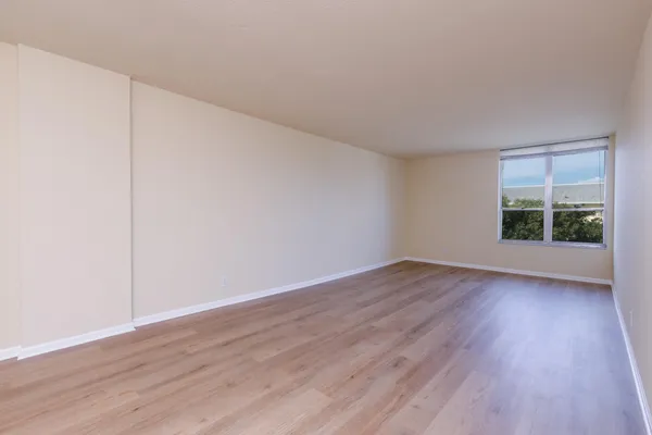 a view of an empty room with wooden floor and a window