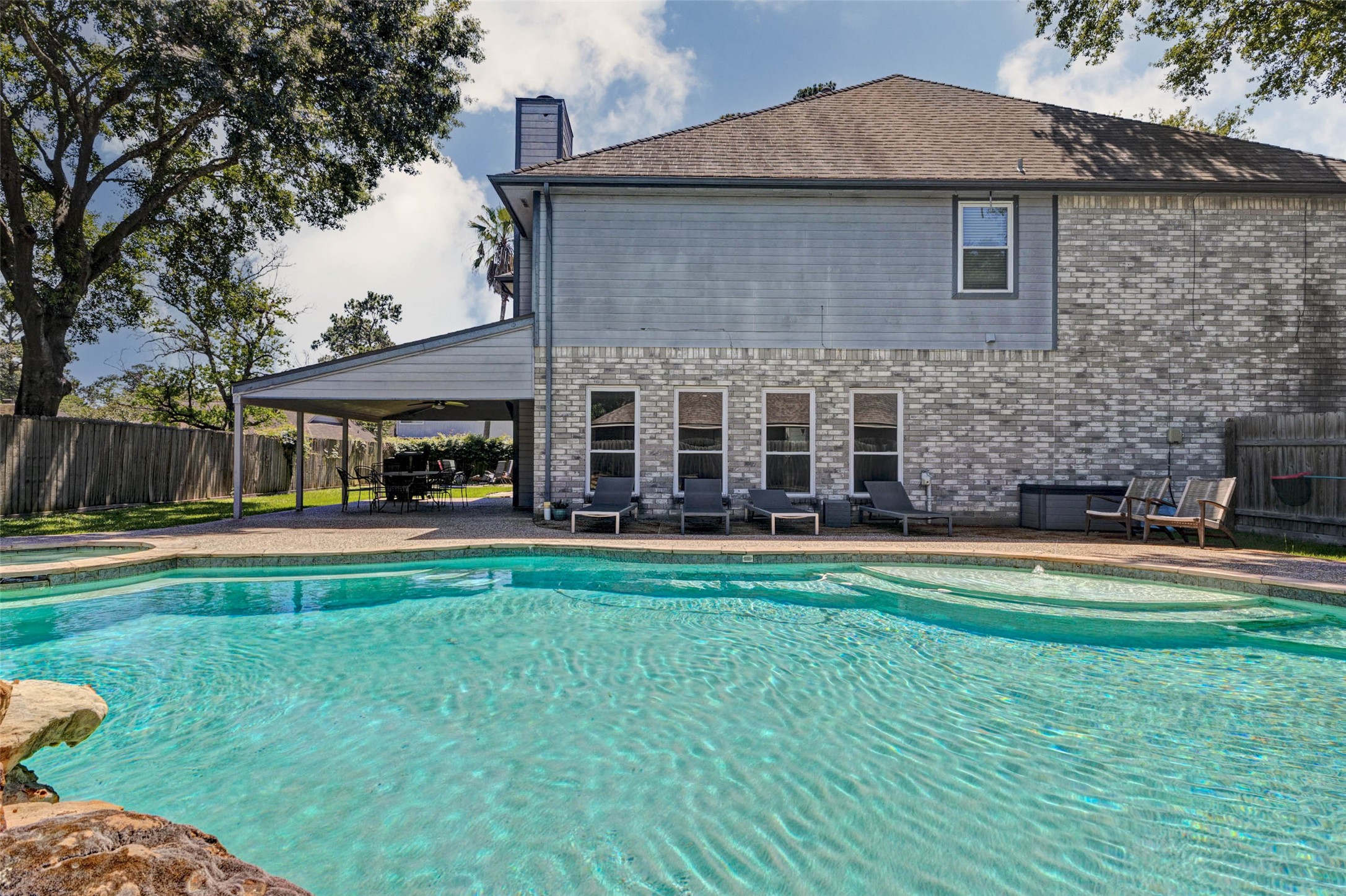 9215 Landry Boulevard Spring, TX 77379 - Photo 37 of 42 An expansive poolside deck lines the side of the home, offering plenty of space for lounge chairs, sunbathing, and outdoor relaxation. The covered patio and additional seating areas create the perfect setup for entertaining guests or enjoying a resort style atmosphere right at home.