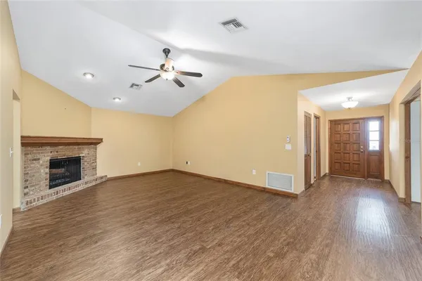 an empty room with chandelier fan and wooden floor