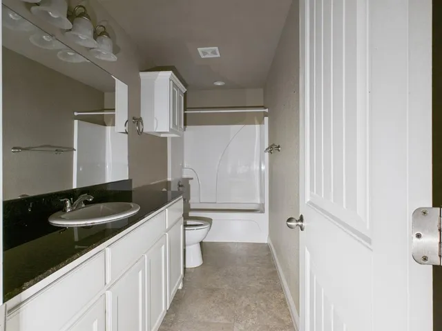 a bathroom with a granite countertop sink a toilet a mirror and shower