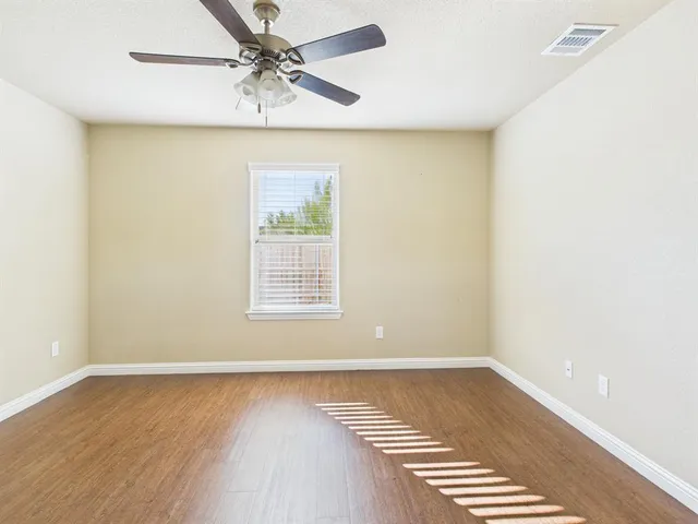 an empty room with wooden floor ceiling fan and windows