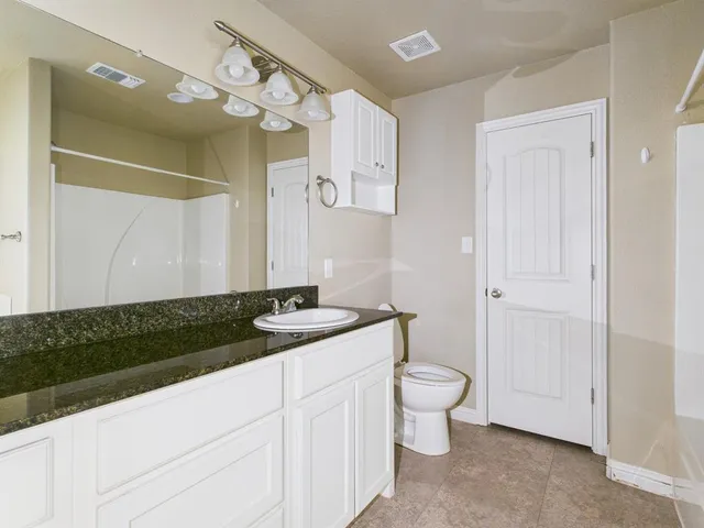 a bathroom with a granite countertop sink a toilet a mirror and vanity