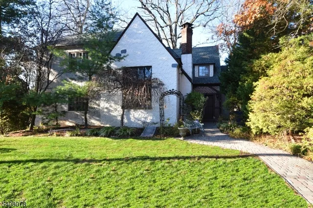 a pathway of a house with potted plants and large trees