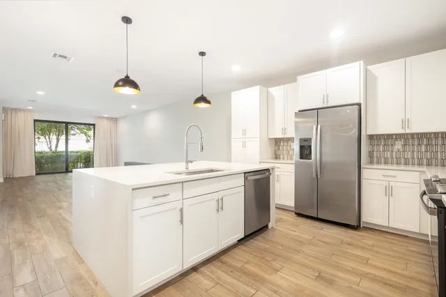 a kitchen with stainless steel appliances granite countertop a refrigerator a sink dishwasher a oven with white cabinets and wooden floor