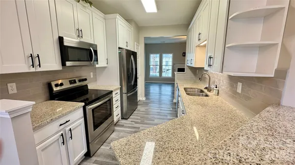 a kitchen with granite countertop a sink a stove top oven a refrigerator and wooden cabinets