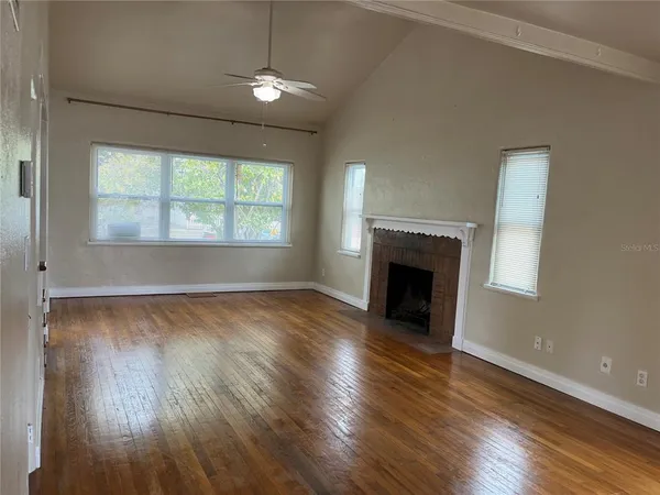 an empty room with wooden floor fireplace and windows