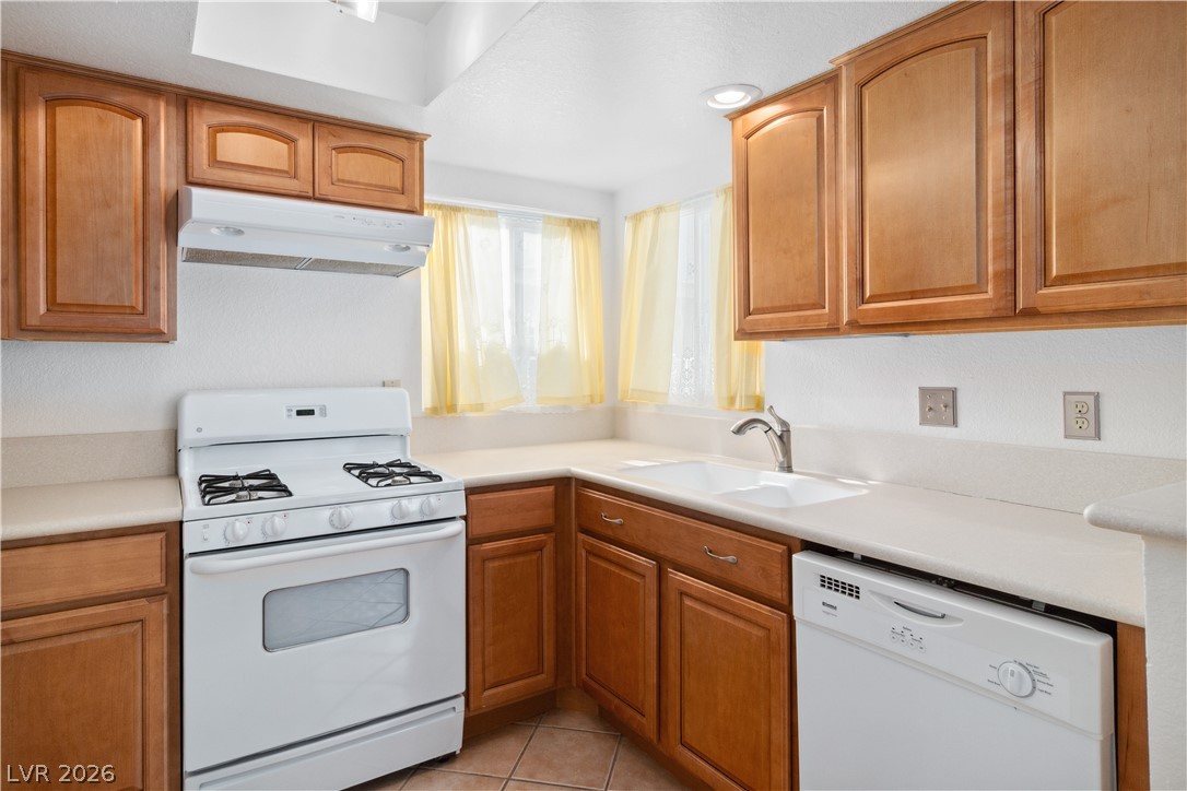 2146 High Dunes Lane Laughlin, NV 89029 - Photo 16 of 64 Kitchen featuring white appliances, under cabinet range hood, light tile patterned flooring, a sink, and brown cabinets