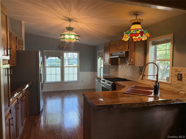 a kitchen with stainless steel appliances granite countertop a refrigerator a sink dishwasher a stove and white countertops with wooden floor