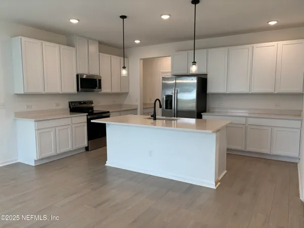 a kitchen with stainless steel appliances granite countertop a sink a stove a refrigerator and white cabinets