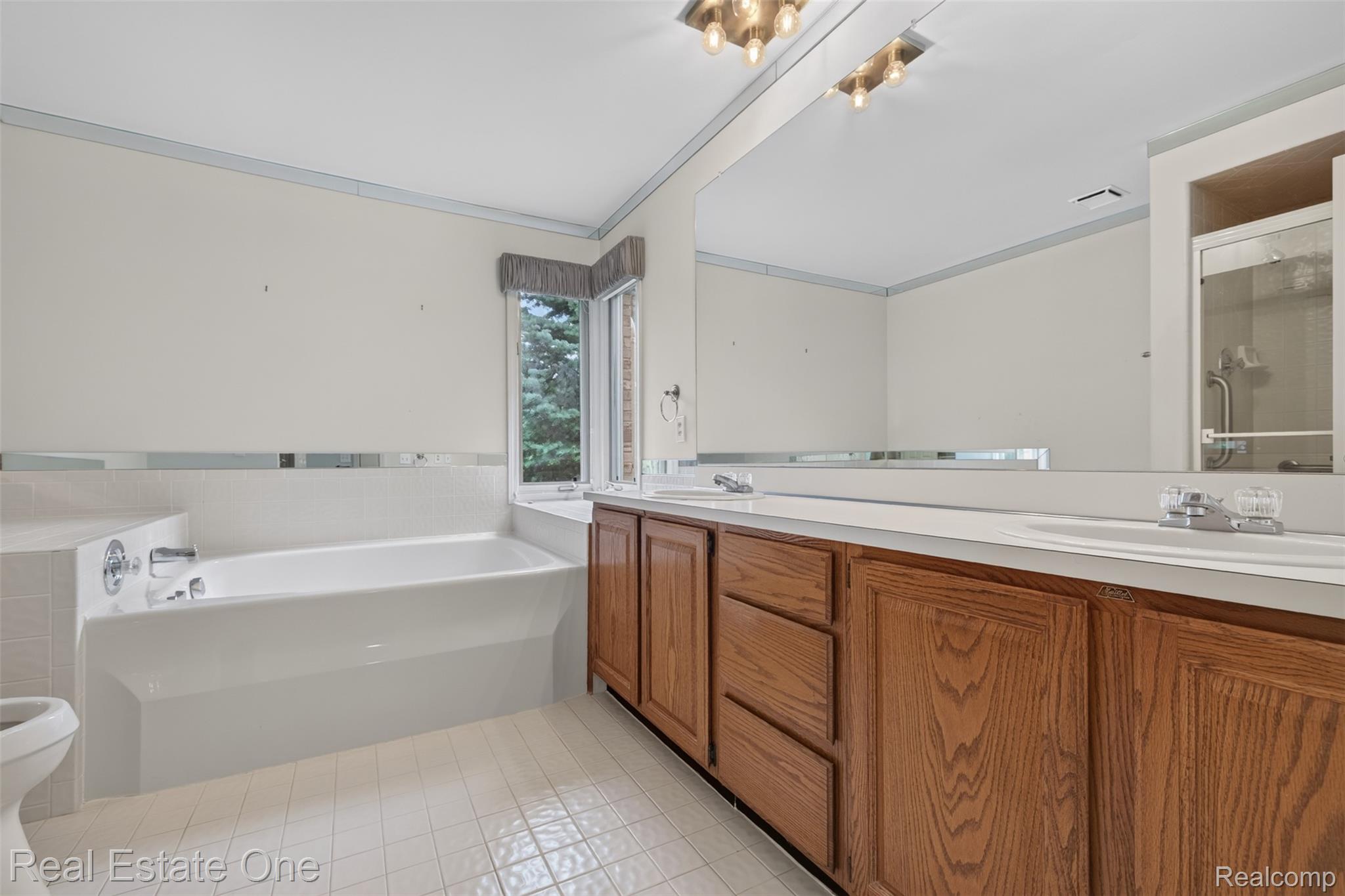 3400 Wedgewood Drive Rochester, MI 48306 - Photo 34 of 49 Bathroom featuring a built-in tub, dual sink vanity with wood cabinetry, and natural light