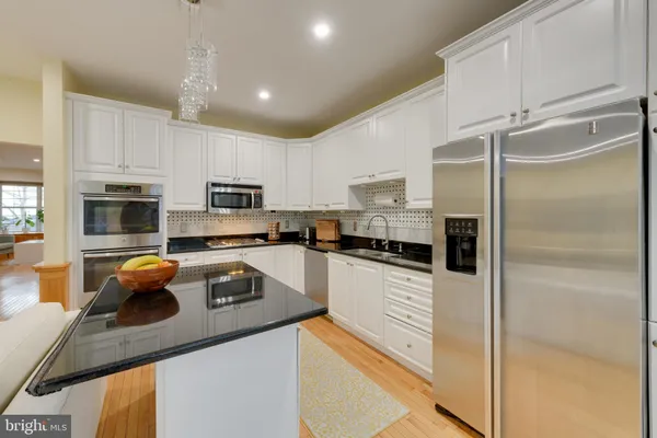 a kitchen with stainless steel appliances granite countertop a refrigerator a sink and white cabinets