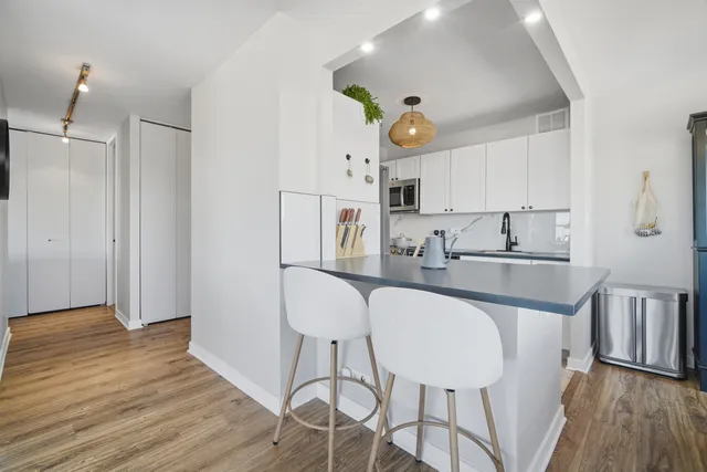 a kitchen with stainless steel appliances a dining table chairs and a refrigerator a sink with wooden floor