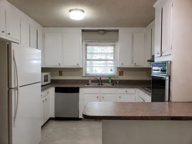 a kitchen with granite countertop a refrigerator sink and white cabinets