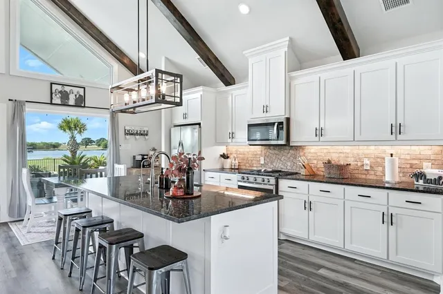 a kitchen with stainless steel appliances kitchen island granite countertop a stove a sink and white cabinets with wooden floor
