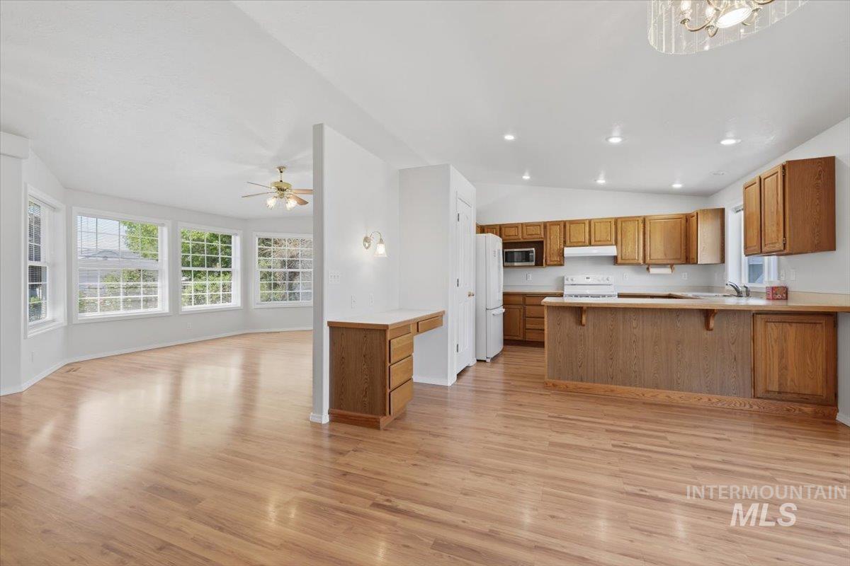 1128 West State Street Meridian, ID 83642 - Photo 12 of 50 Open-concept living area featuring wood-finish flooring, a kitchen with wood cabinetry and white appliances, recessed lighting, and a dining area with a curved wall of multiple windows