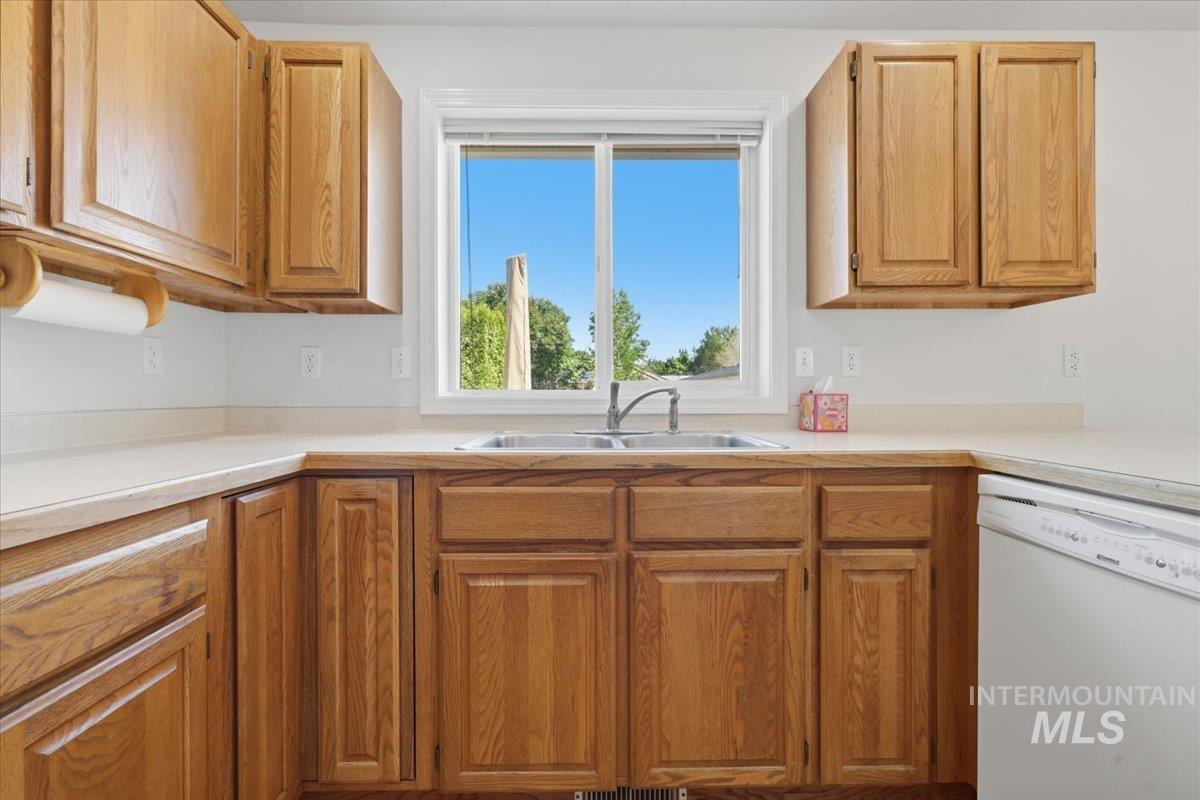 1128 West State Street Meridian, ID 83642 - Photo 19 of 50 Kitchen featuring wood-finish cabinetry, light-toned countertops, a stainless steel double basin sink, and a white built-in dishwasher