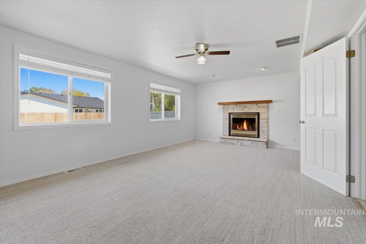 1128 West State Street Meridian, ID 83642 - Photo 22 of 50 Spacious room featuring light-colored carpet flooring, multiple windows providing natural illumination, and a stone-clad fireplace with a wood mantel