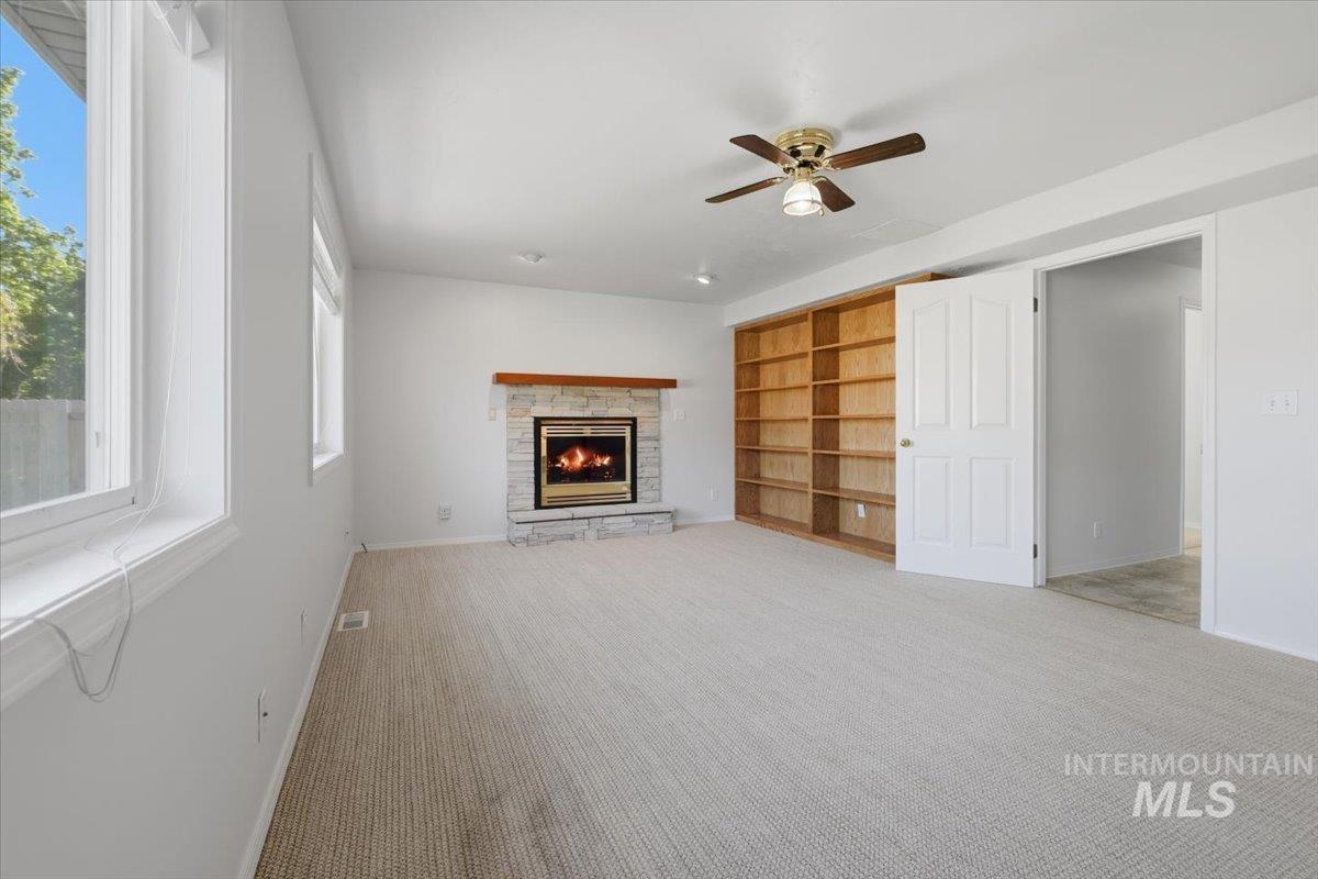 1128 West State Street Meridian, ID 83642 - Photo 24 of 50 Spacious living area featuring a stone-faced fireplace with wood mantel, built-in shelving, light-toned carpeting, and a ceiling fan