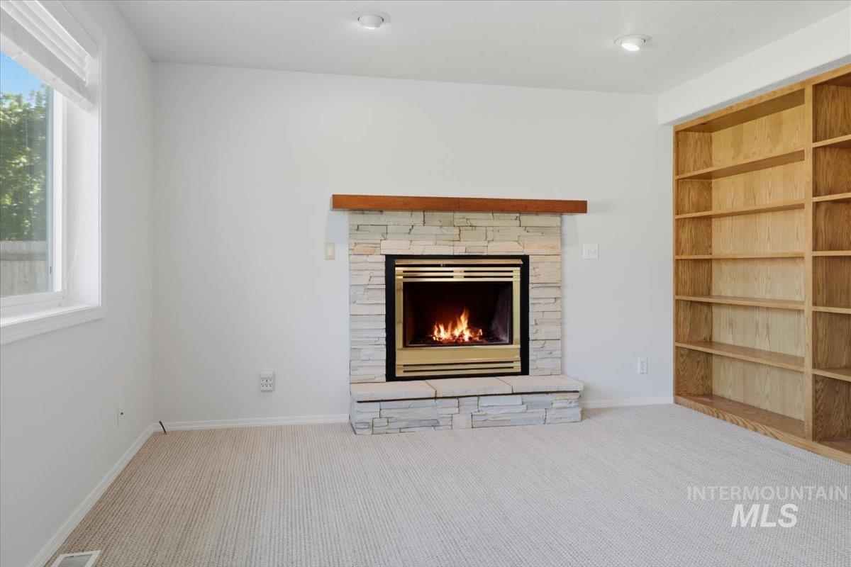 1128 West State Street Meridian, ID 83642 - Photo 25 of 50 Living area featuring a gas fireplace with a stone surround and wood mantel, built-in natural wood shelving, recessed lighting, and carpet flooring