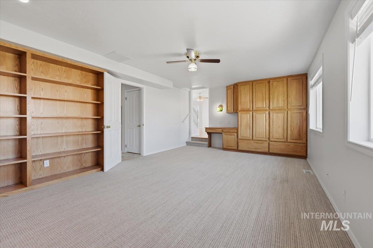 1128 West State Street Meridian, ID 83642 - Photo 26 of 50 Spacious carpeted room featuring extensive built-in wooden shelving, a comprehensive built-in wooden cabinetry unit with an integrated desk, and multiple windows providing natural light