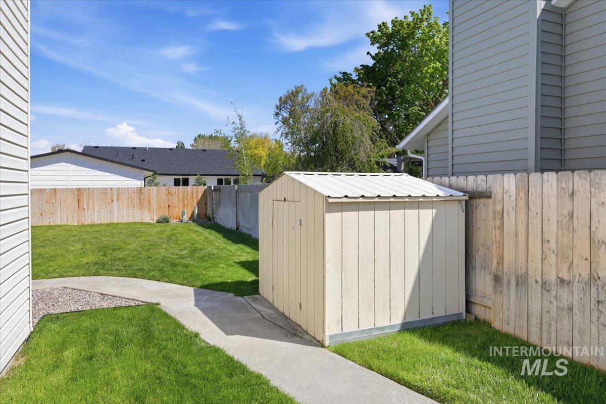 1128 West State Street Meridian, ID 83642 - Photo 44 of 50 Expansive backyard featuring a storage shed with a metal roof, a concrete pathway, a manicured lawn, and wood privacy fencing
