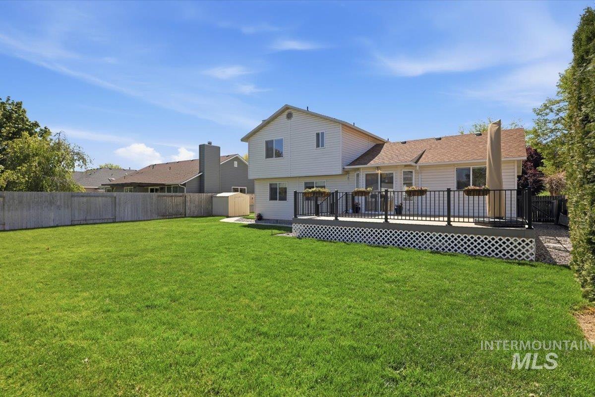 1128 West State Street Meridian, ID 83642 - Photo 45 of 50 Expansive green lawn with a wooden privacy fence, leading to a raised outdoor deck featuring black railings and white lattice skirting