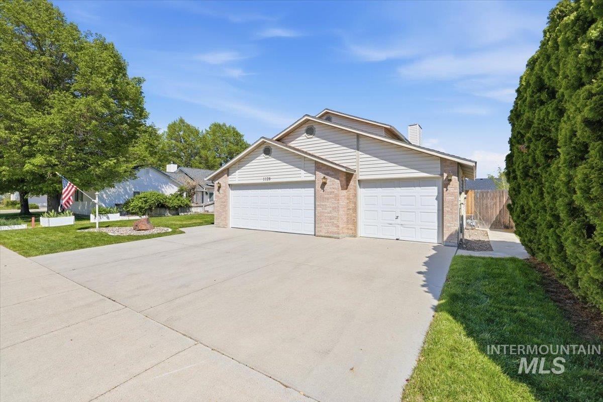 1128 West State Street Meridian, ID 83642 - Photo 5 of 50 Brick and siding exterior featuring two attached garage doors, a concrete driveway, and a manicured lawn with mature trees and shrubs