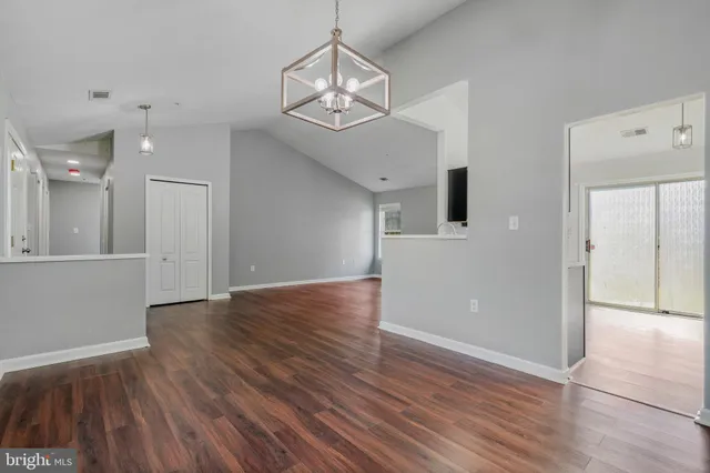 a view of an empty room with wooden floor and a kitchen